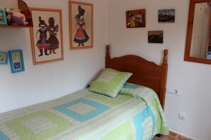 Quarto com cama de madeira, colcha e quadros nas paredes.