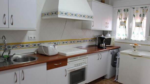 A kitchen with white cabinets, a wooden countertop, a sink, a stove, a microwave, and a refrigerator.