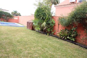 Uma área residencial com piscina, um pequeno depósito e diversos tipos de plantas ao longo da parede.