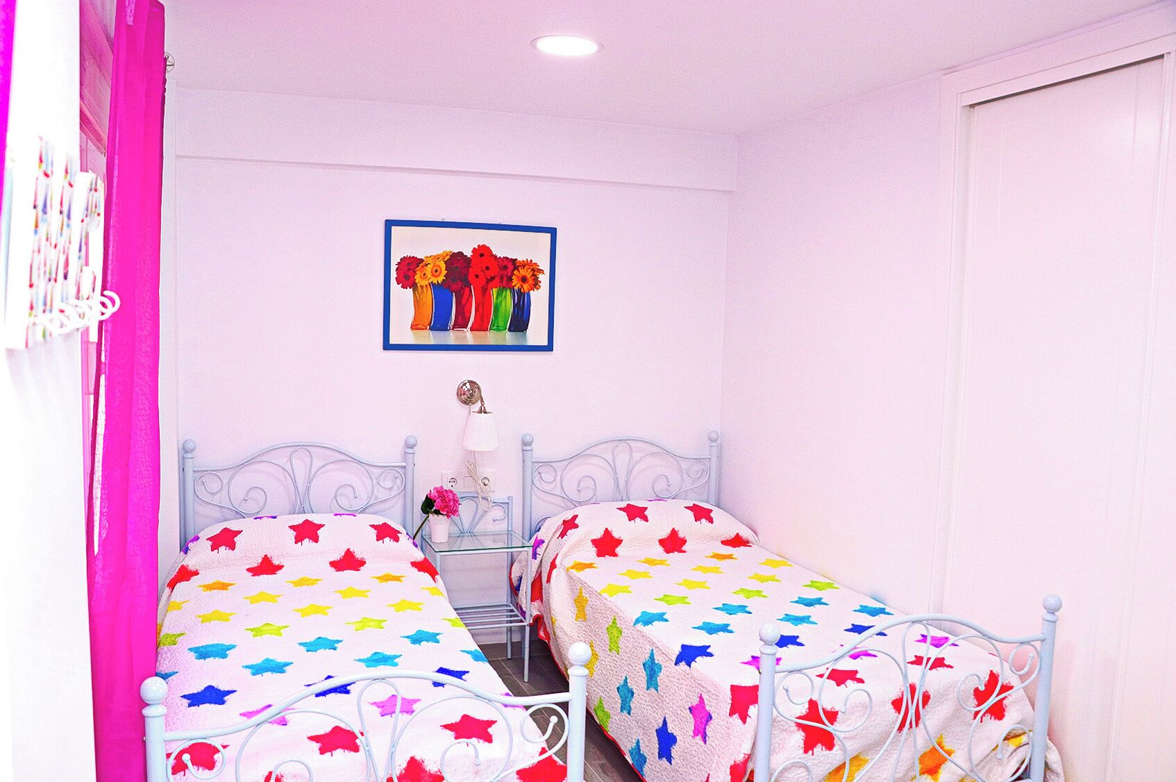 A bedroom with two beds, each with a star-patterned bedspread, a bedside table with a lamp, and a framed picture on the wall.