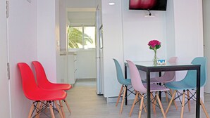 Un comedor moderno con una mesa y sillas coloridas, un televisor de pantalla plana en la pared, y vistas al exterior a través de una puerta.