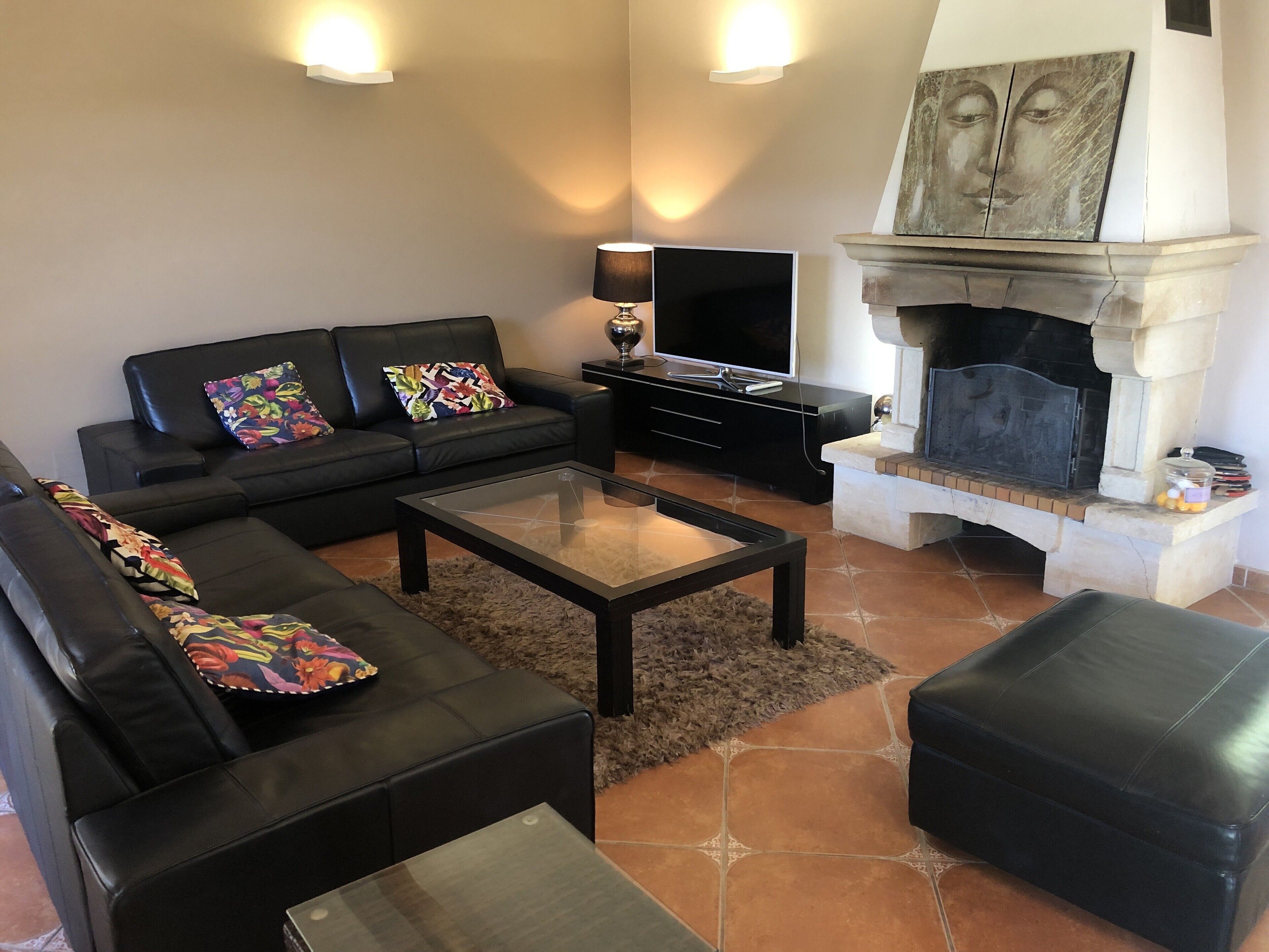 A living room with a black sofa, a glass coffee table, a fireplace, and a television.