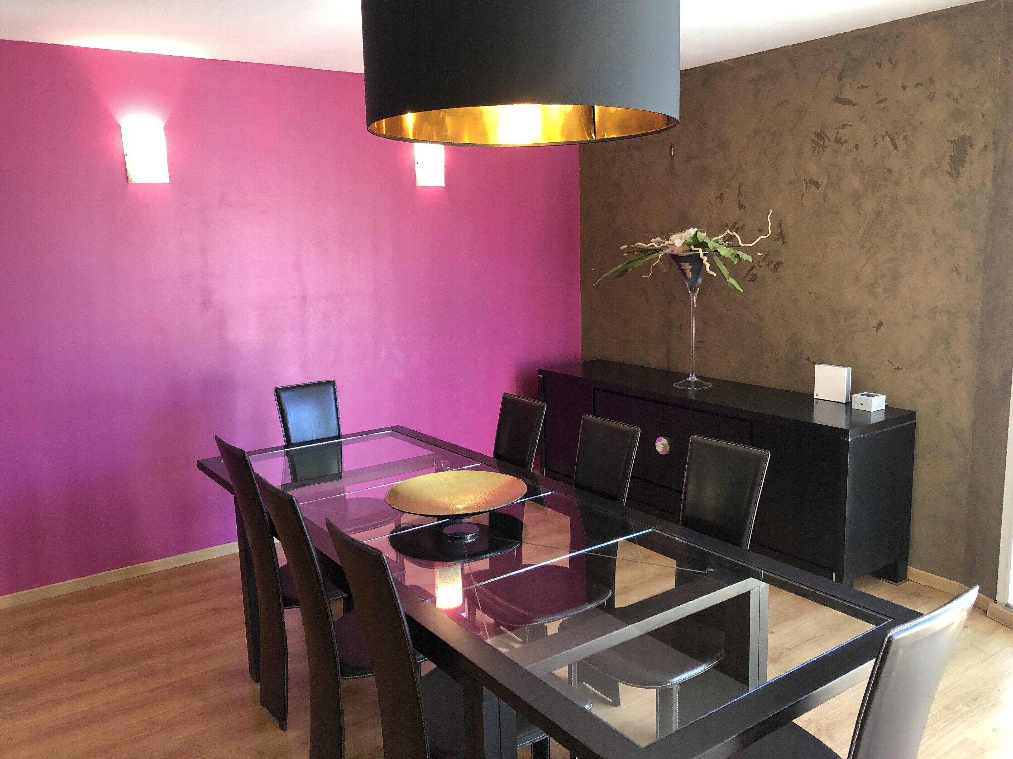 Un comedor moderno con una mesa de vidrio, sillas negras, un armario negro y una pared rosa.