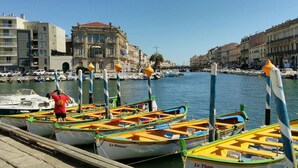 A marina with colorful boats docked, a person in a red shirt, and historic buildings in the background. - Hacienda : 220m2 villa for 12 people with swimming pool, 5 minutes from the beach (Vic La Gardiole)