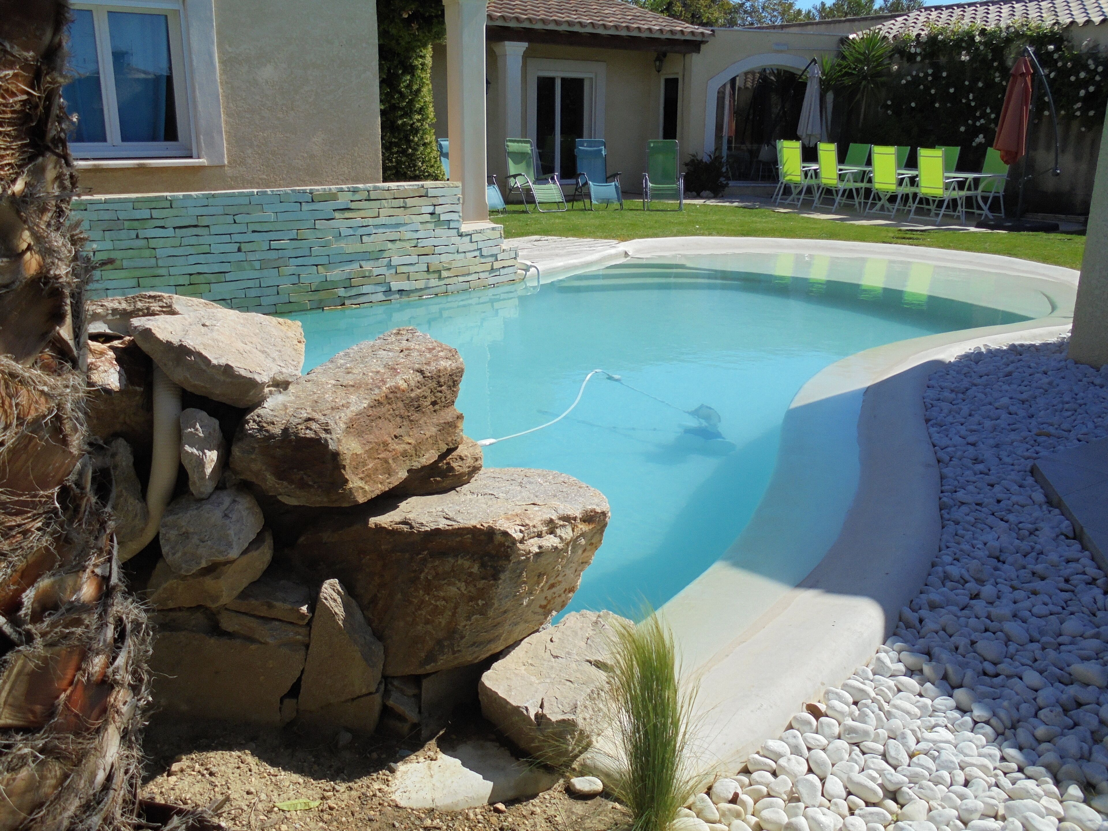 A swimming pool with a stone border, surrounded by white pebbles and a few rocks.