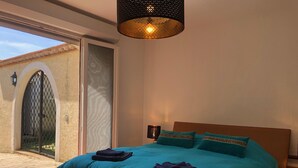 A bedroom with a large bed, a nightstand, a hanging light fixture, and a view of the outside. - Hacienda : 220m2 villa for 12 people with swimming pool, 5 minutes from the beach (Vic La Gardiole)