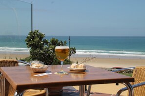 A table with a glass of wine, a basket of bread, and a plate of food, overlooking a beach with the ocean and a clear sky. - Holiday apartment, pets welcome too (CONIL DE LA FRONTERA)