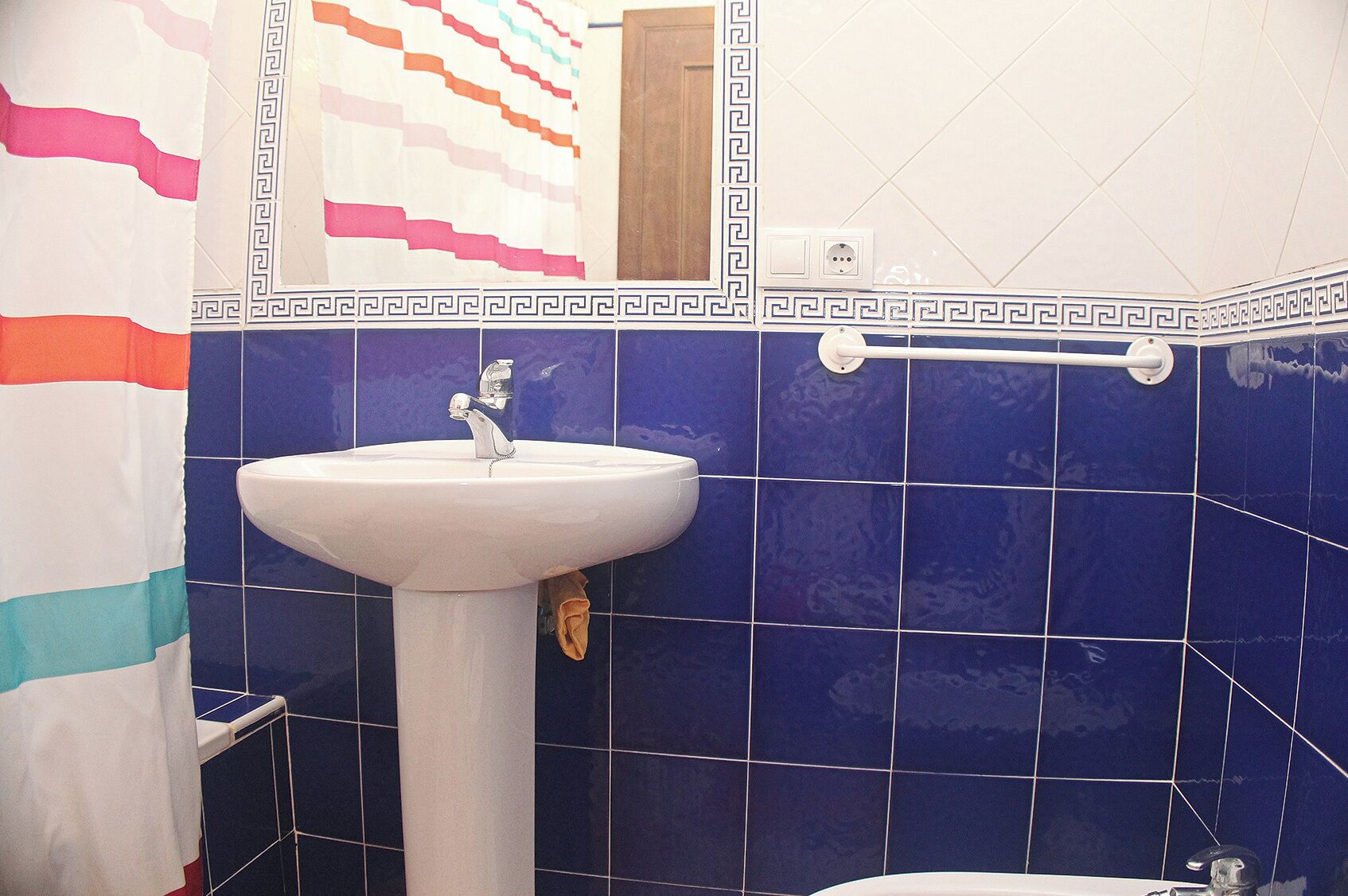 Une salle de bain avec un lavabo blanc, des carreaux bleus et un porte-serviettes.