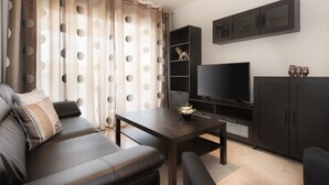 A modern living room with a dark leather sofa, a coffee table, a flat-screen TV, dark cabinets, and a decorative shelf with a figurine. - Holiday Rental Apartment with wifi (Marbella)