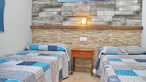 Una habitación con dos camas, cada una con colcha acolchada, una mesita de noche de madera y una lámpara fijada a la pared.