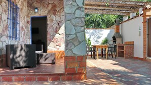 Un patio con muros de piedra, una columna de ladrillo, una parrilla y mobiliario exterior.