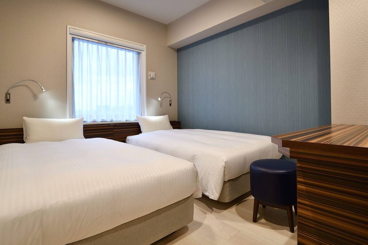 A hotel room with two beds, a desk, and a window with curtains.