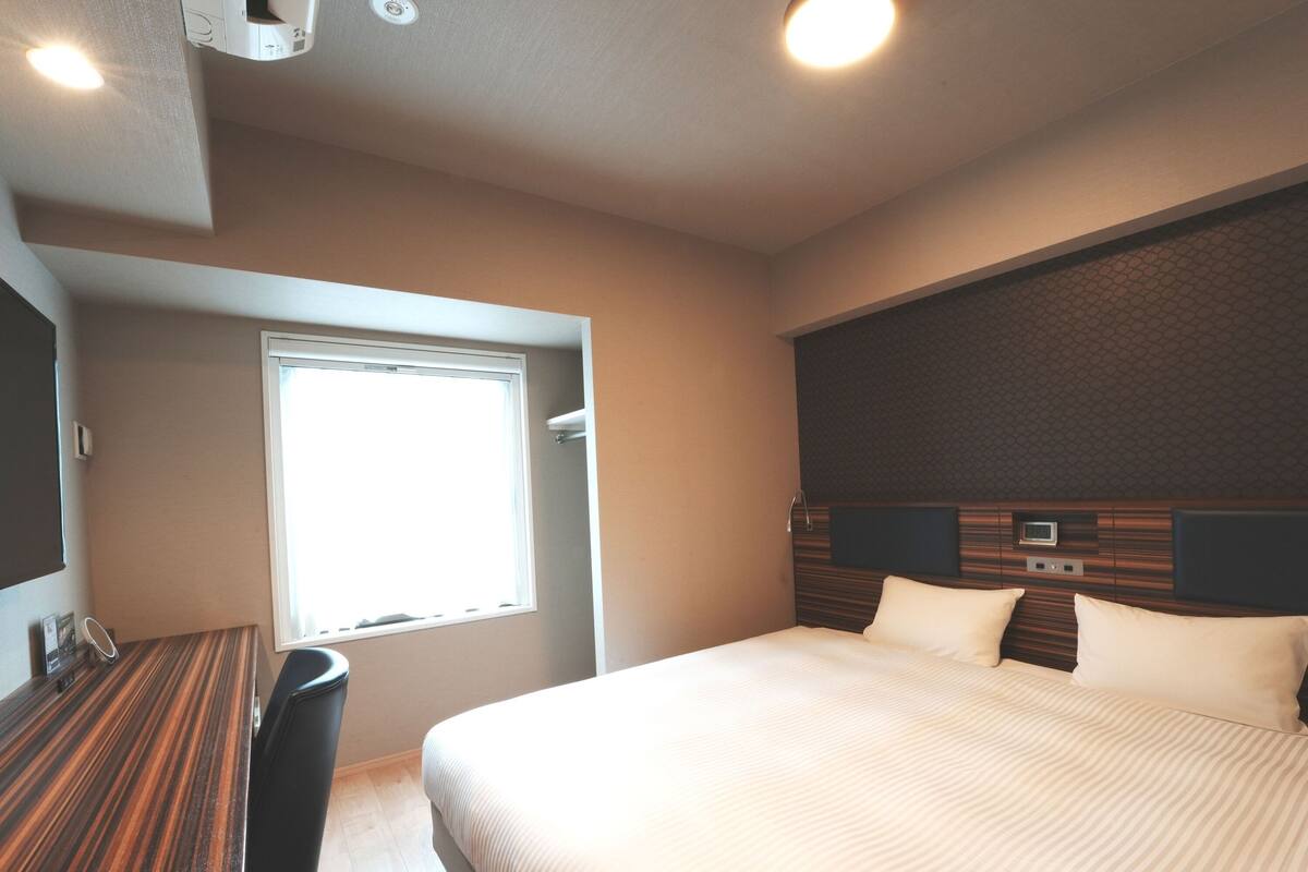 A hotel room with a large bed, a desk, and a window.