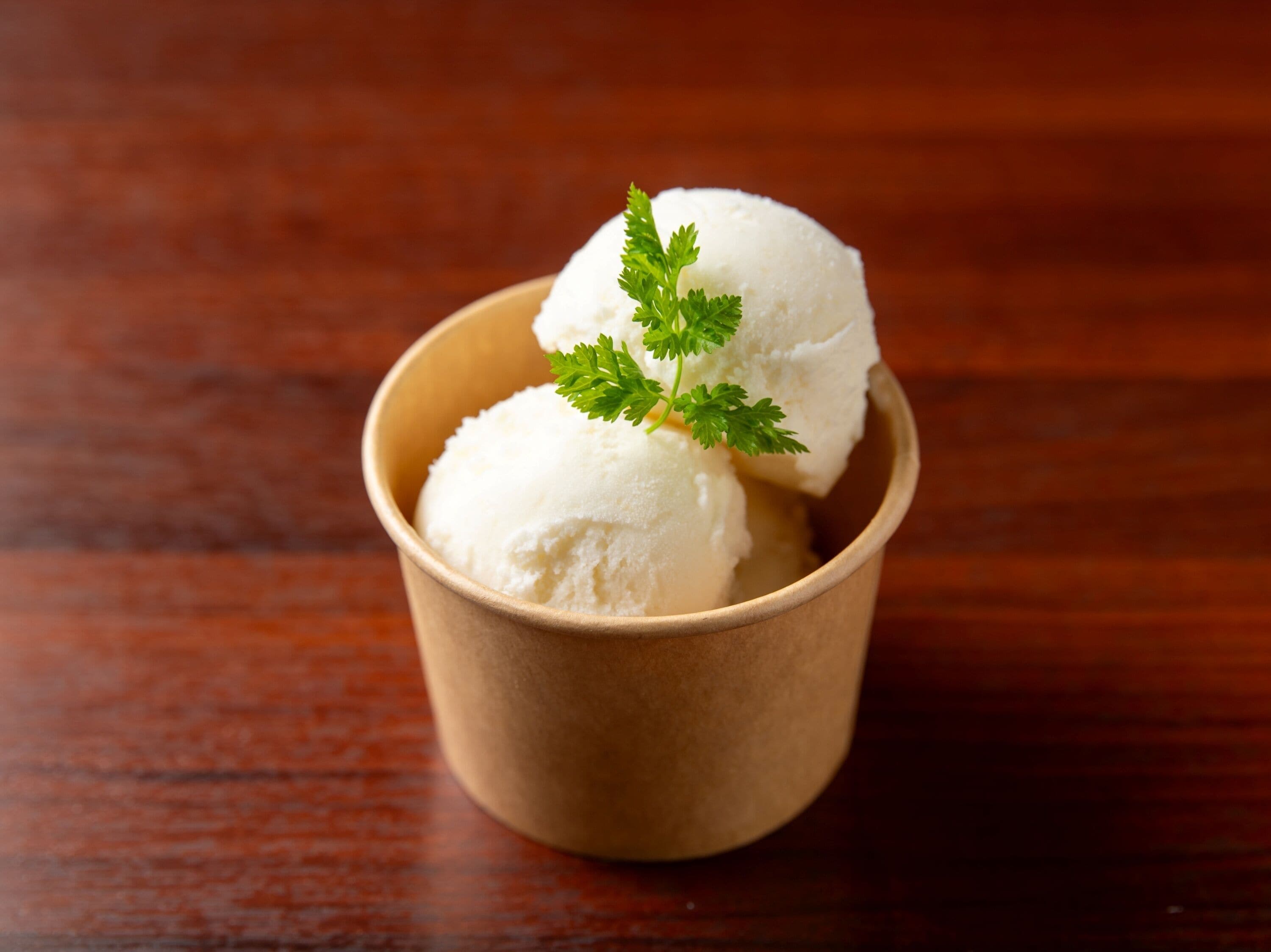 A wooden bowl containing two scoops of white ice cream garnished with a sprig of parsley.