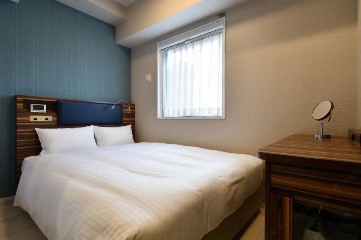 A hotel room with a bed, bedside table, and a window.