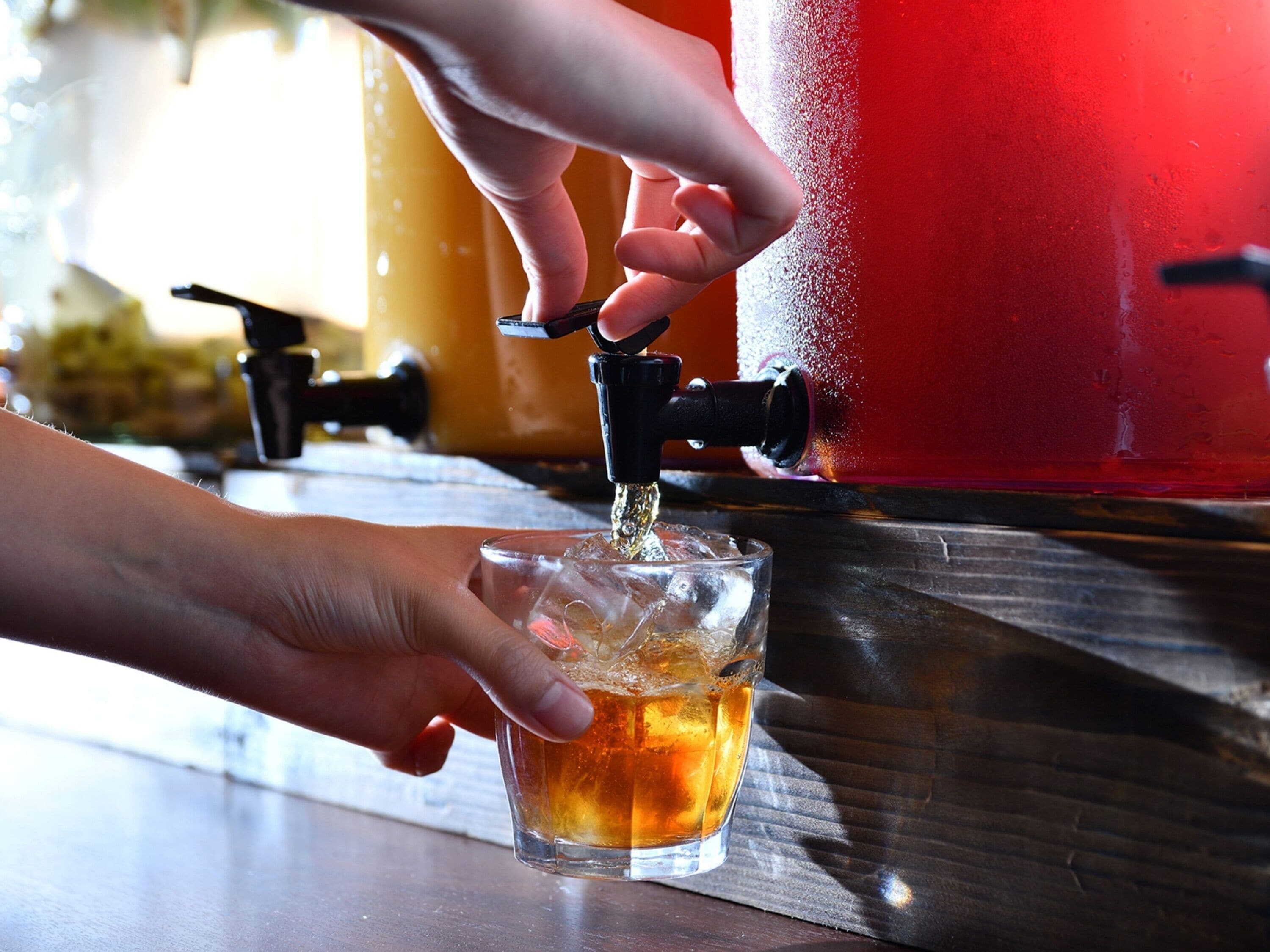 Een hand giet een drankje uit een kraan in een glas.