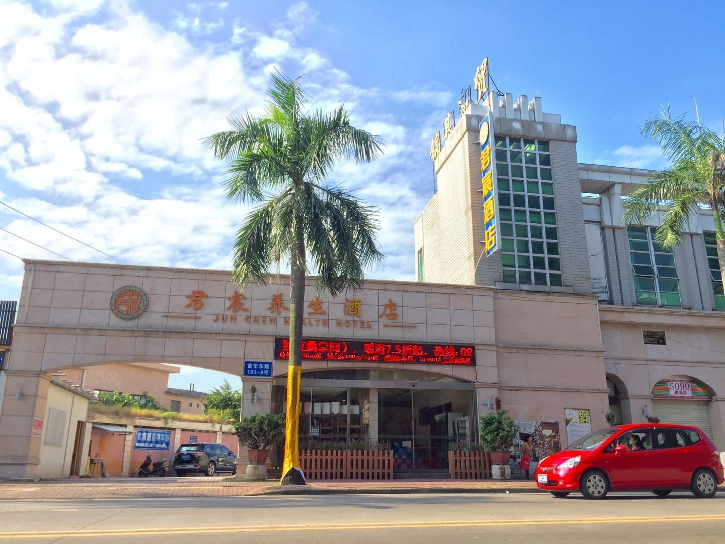 A hotel with a prominent sign, a palm tree, and a red car parked in front.