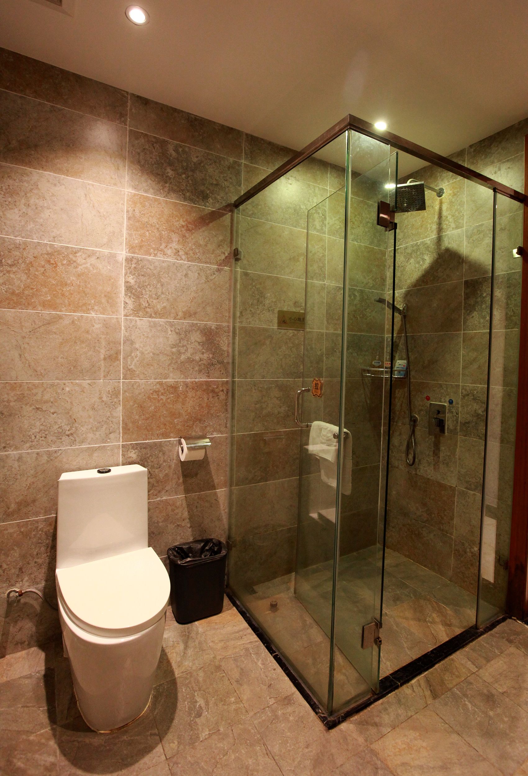 A modern bathroom with a glass-enclosed shower, a toilet, and a trash bin.