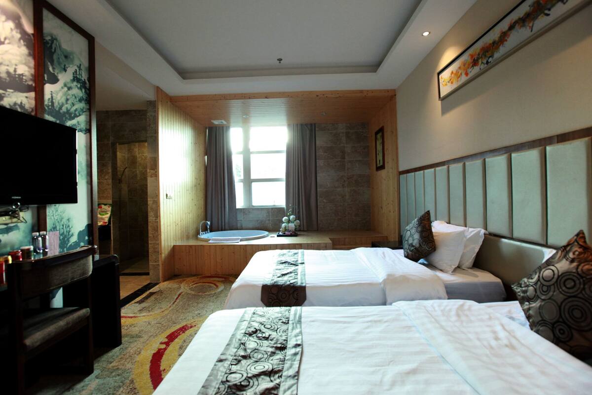 A hotel room with two beds, a television, a desk, and a large window.