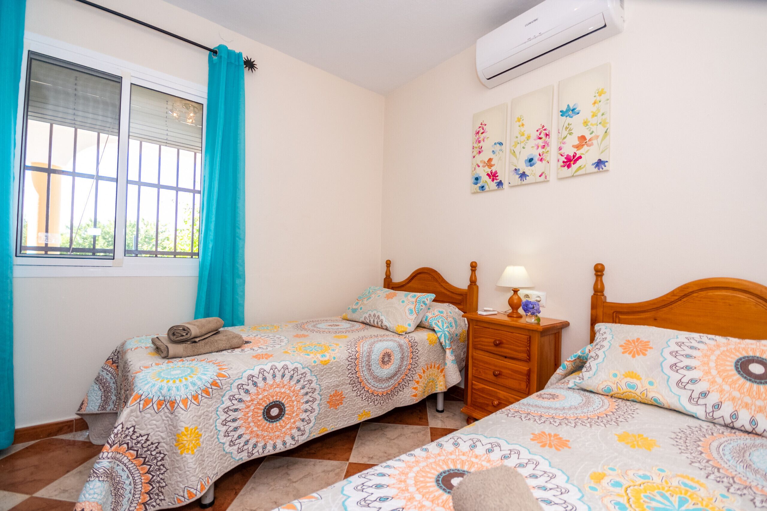 Une chambre avec deux lits, une fenêtre avec des rideaux, un climatiseur et une table de chevet avec une lampe.
