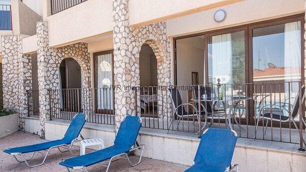 A balcony with blue lounge chairs, stone pillars, and a view of the street. - An apartment that sleeps 4 guests  in 2 bedrooms (Ayia Napa)