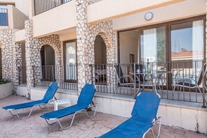 A balcony with blue lounge chairs, stone pillars, and a view of the street.