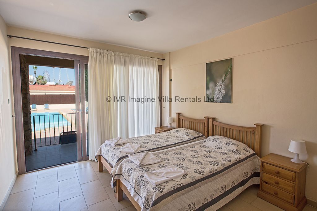 Quarto com duas camas, um quadro na parede e vista para uma piscina através de uma porta aberta.