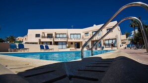A poolside view of a villa complex with a clear blue sky, a swimming pool, and lounge chairs. - An apartment that sleeps 4 guests  in 2 bedrooms (Ayia Napa)