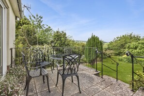 A patio with a table and chairs, surrounded by a garden and a view of the countryside. - Meadow View, Blue Anchor (Blue Anchor)