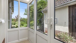 A conservatory with large glass doors, a tiled floor, and a view of greenery and a brick wall outside. - Meadow View, Blue Anchor (Blue Anchor)
