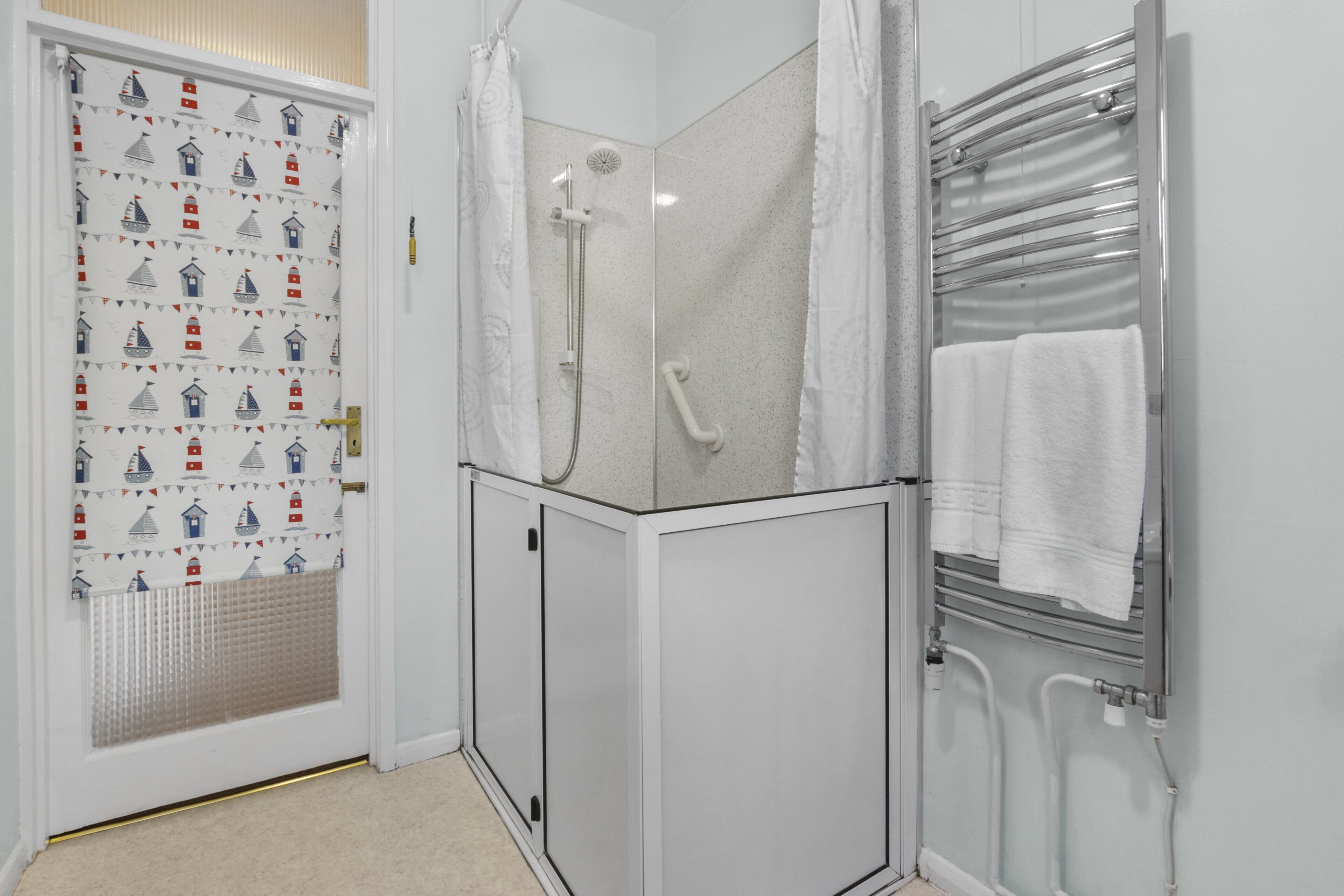 A bathroom with a shower, a towel rack, and a door with a nautical-themed curtain.