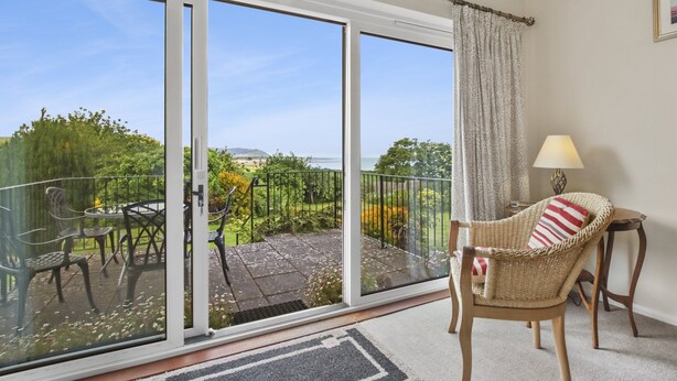 A balcony with a view of a garden and sea, a wicker chair, and a small table with a lamp. - Meadow View, Blue Anchor (Blue Anchor)