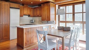 A kitchen with wooden cabinets, a white refrigerator, a sink, and a dining area with white chairs and a table. - Val de Ruda 46 by FeelFree Rentals (Naut Aran)