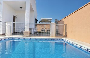 A swimming pool with tiled edges, surrounded by a white building with a beige wall, and metal gates.