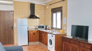 A compact kitchen with a washing machine, microwave, and a TV on a wooden cabinet.