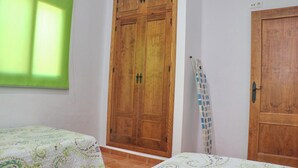 A bedroom with two beds, a wooden wardrobe, and a window with blinds.