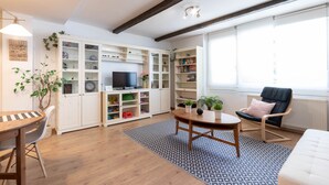 Een moderne woonkamer met houten vloer, een rond bijzettafeltje, een bank, een boekenkast en een televisie.