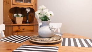 Een eettafel met een witte bloevas, zwart-wit gestreepte placemats en een houten kast op de achtergrond.