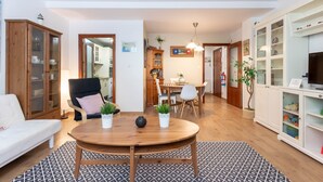 Een woonkamer met een bank, een eettafel met stoelen, een houten kast en een televisie.