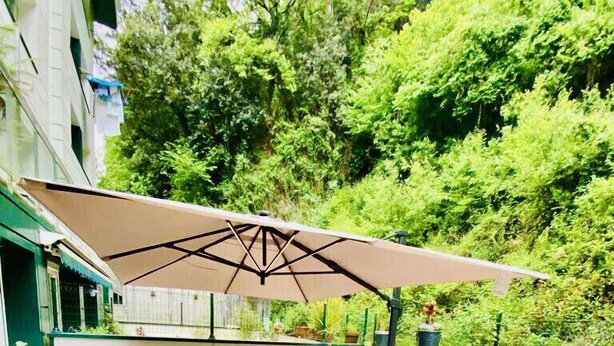 Een terras buiten met een grote parasol, zitgedeelte en plantenpotten.