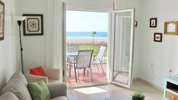 A living room with a sofa, a coffee table, and a balcony with a table and chairs. - Apartment in Conil amazing beach views (CONIL DE LA FRONTERA)