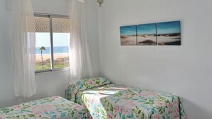 A bedroom with two beds, a window with beach view, and a painting on the wall. - Apartment in Conil amazing beach views (CONIL DE LA FRONTERA)