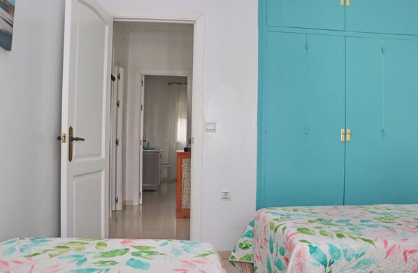 A bedroom with two beds, a bathroom visible through an open door, and a teal wardrobe.