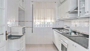 A kitchen with white cabinets, a microwave, a sink, and a window with a curtain. - Apartment in Conil amazing beach views (CONIL DE LA FRONTERA)