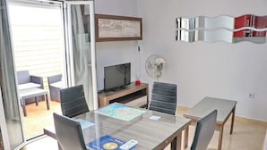 A room with a dining table, chairs, a TV, a fan, and a sliding glass door leading to an outdoor seating area.