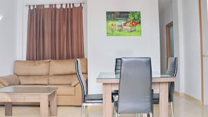 A living room with a beige sofa, a glass-top dining table, and two black chairs.
