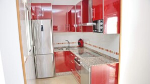 A compact kitchen with red cabinets, a stainless steel refrigerator, a microwave, and a sink.