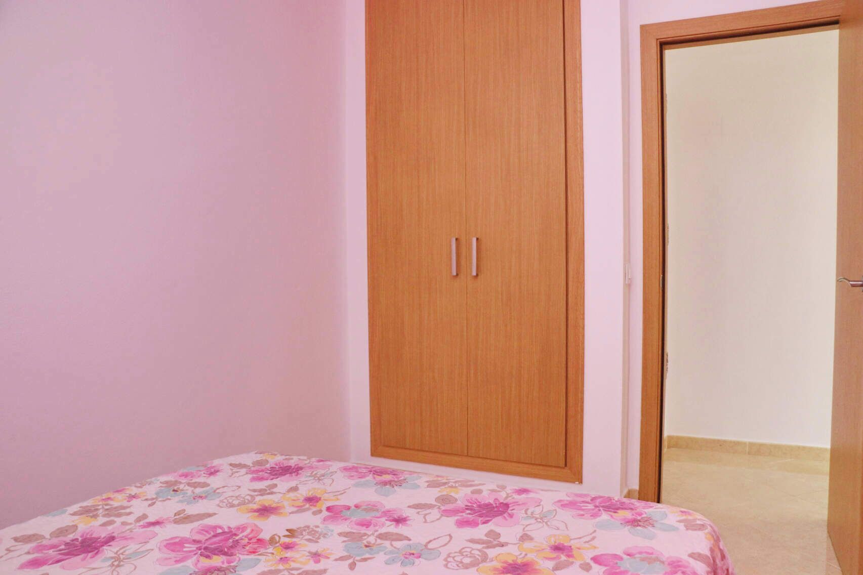 A bedroom with a bed, a wooden wardrobe, and a door.