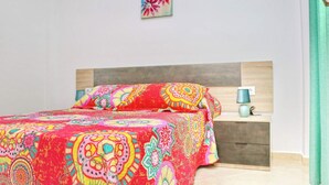 A bed with a colorful patterned bedspread, a bedside table with a lamp, and a small wall art piece above the bed.