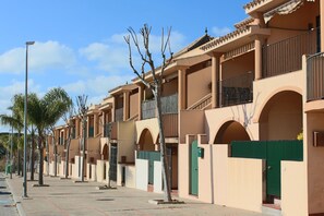 Une rangée d’immeubles à plusieurs étages dotés de balcons, un ciel dégagé et un trottoir.
